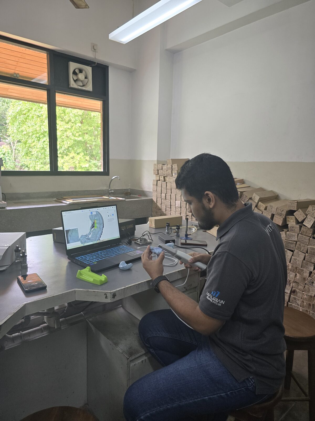 A team member scanning a dental cast with a handheld scanner while monitoring the live point cloud on a laptop